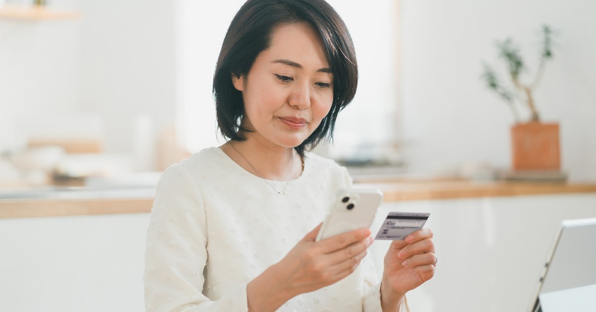 スマートフォンとクレジットカードを手に持ち支払いの登録をする女性