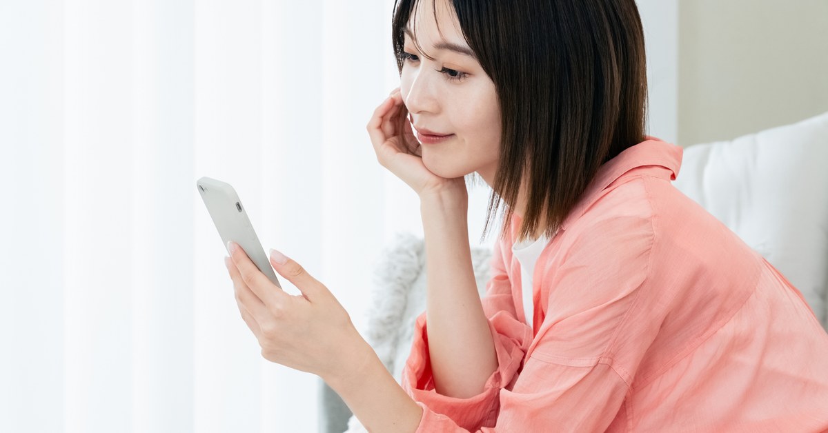 窓辺でスマートフォンを見る女性