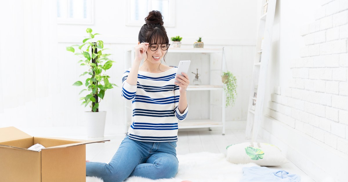 段ボール箱のそばでスマートフォンを見る女性