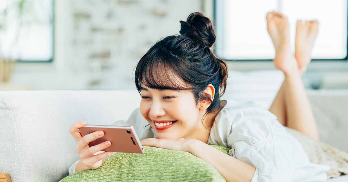 ソファでくつろぎながらスマートフォンで動画を見る女性